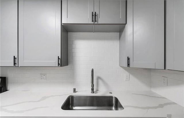 kitchen featuring light stone countertops, gray cabinetry, sink, and tasteful backsplash