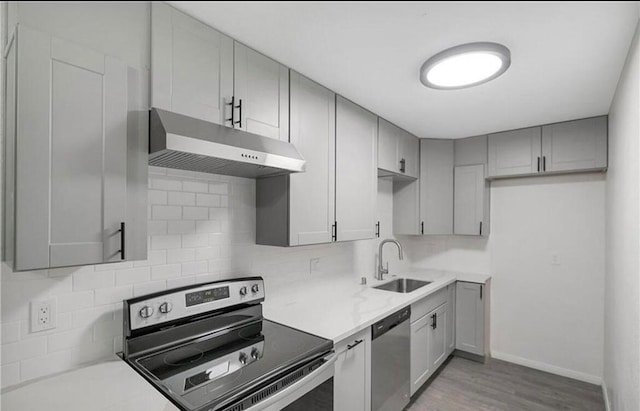 kitchen featuring sink, gray cabinetry, stainless steel appliances, light wood-type flooring, and decorative backsplash