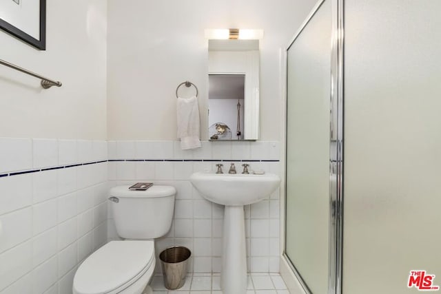 bathroom with tile walls, toilet, a shower with door, and tile patterned floors