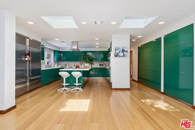 kitchen featuring a center island, light hardwood / wood-style flooring, backsplash, a skylight, and built in fridge