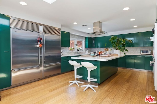 kitchen with built in fridge, light hardwood / wood-style flooring, green cabinets, and island range hood