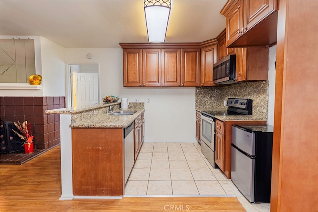 kitchen with light hardwood / wood-style flooring, light stone counters, sink, stainless steel appliances, and kitchen peninsula