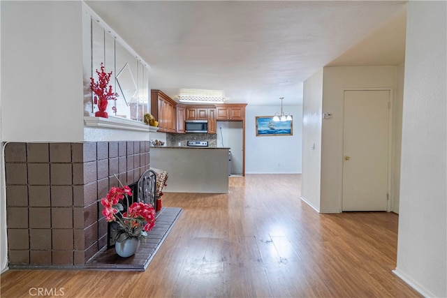 kitchen with kitchen peninsula, tasteful backsplash, stainless steel appliances, a notable chandelier, and light hardwood / wood-style floors