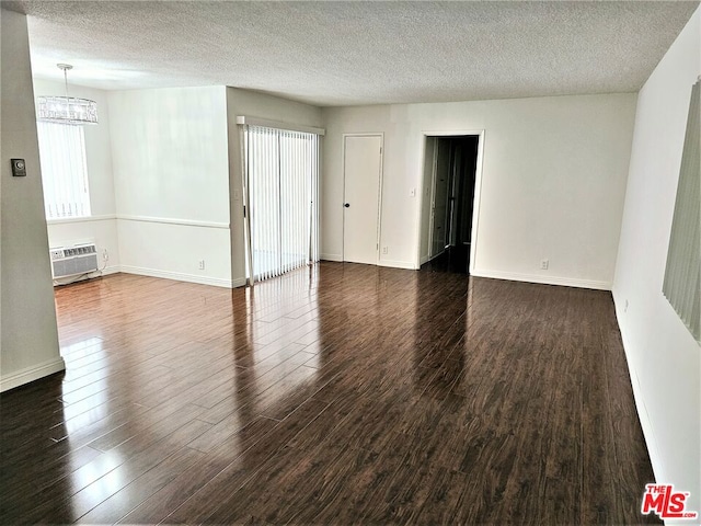 spare room featuring a textured ceiling, an inviting chandelier, dark hardwood / wood-style floors, and a wall mounted AC