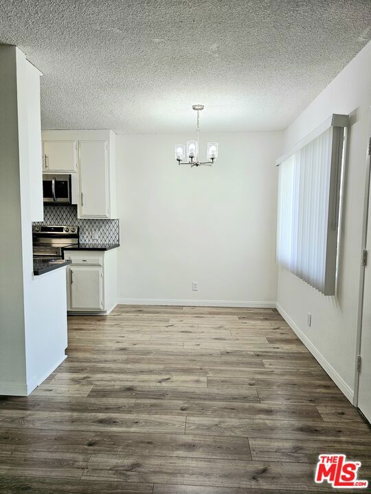 kitchen with hardwood / wood-style flooring, white cabinets, hanging light fixtures, stainless steel appliances, and backsplash