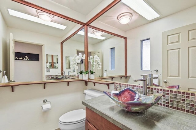 bathroom featuring decorative backsplash, a skylight, vanity, and toilet