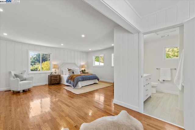 bedroom featuring connected bathroom, multiple windows, and light hardwood / wood-style flooring