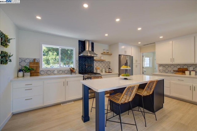 kitchen featuring white cabinetry, wall chimney exhaust hood, light hardwood / wood-style floors, and appliances with stainless steel finishes