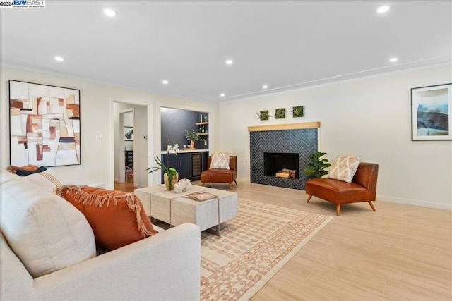 living room featuring a tiled fireplace, ornamental molding, and light hardwood / wood-style flooring