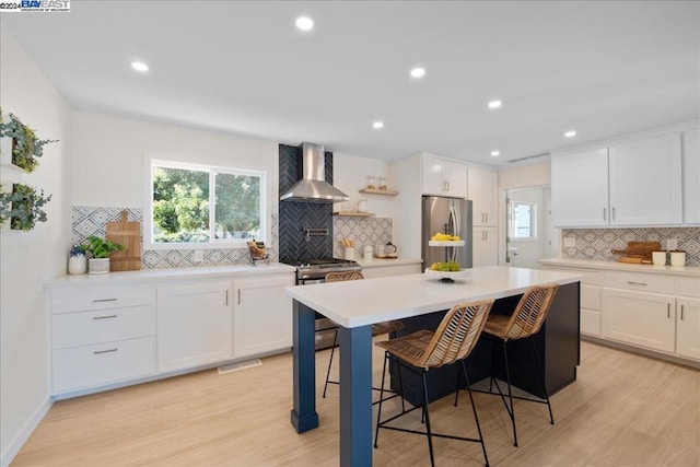 kitchen with white cabinets, appliances with stainless steel finishes, light hardwood / wood-style floors, and wall chimney range hood