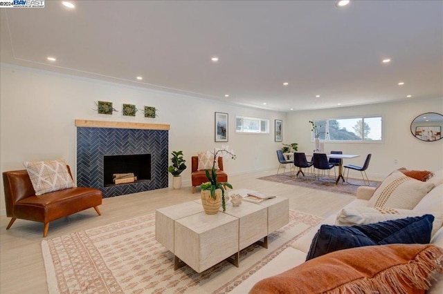 living room featuring light hardwood / wood-style flooring, crown molding, and a tiled fireplace