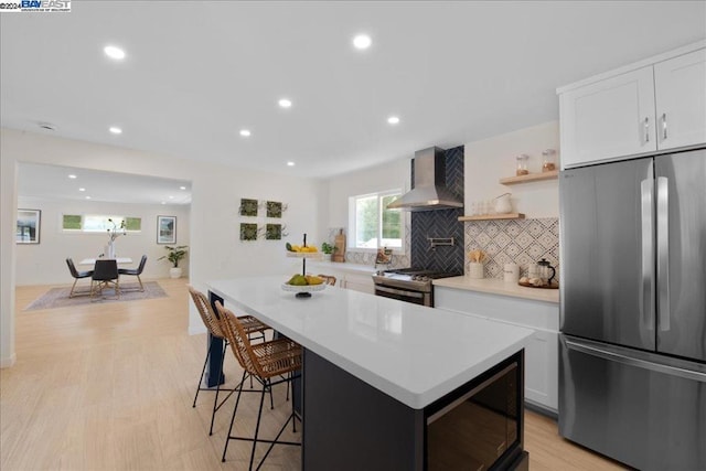 kitchen with white cabinets, wall chimney exhaust hood, light hardwood / wood-style floors, and appliances with stainless steel finishes