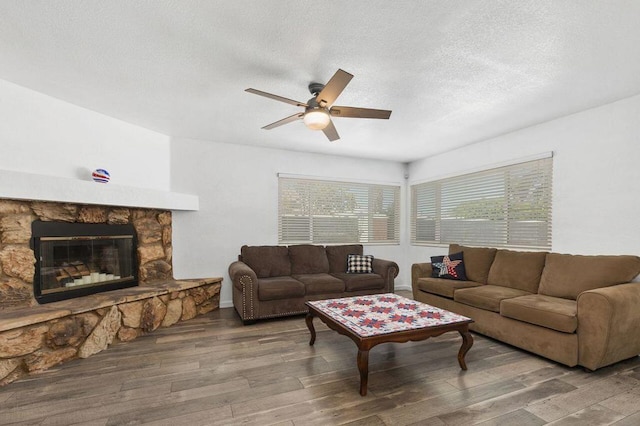 living room featuring ceiling fan, wood-type flooring, a fireplace, and a textured ceiling