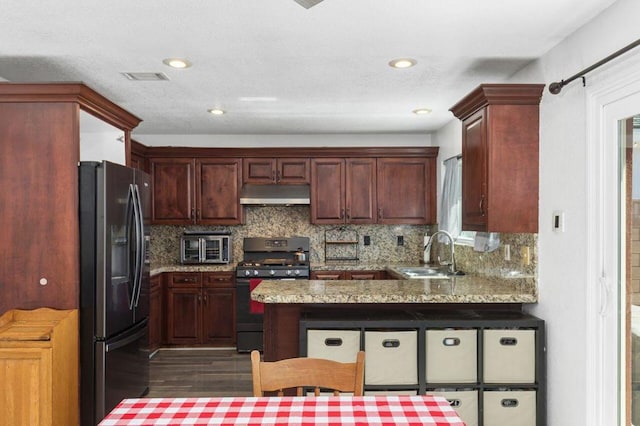 kitchen featuring kitchen peninsula, decorative backsplash, sink, black gas stove, and stainless steel fridge