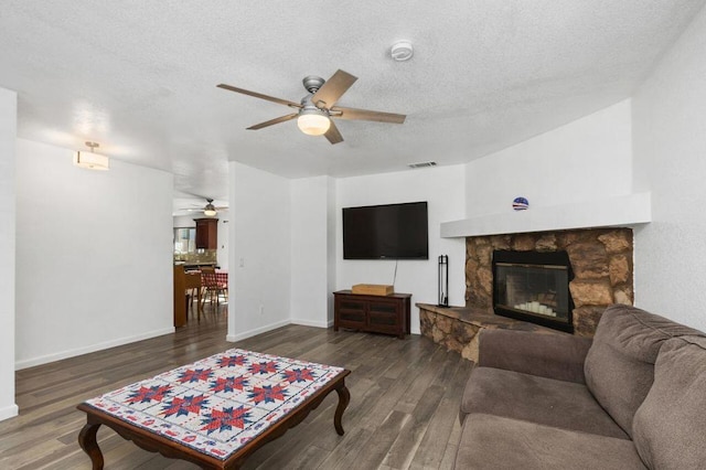 living room featuring ceiling fan, a textured ceiling, dark hardwood / wood-style floors, and a fireplace