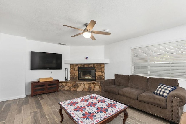 living room with ceiling fan, wood-type flooring, a textured ceiling, and a fireplace