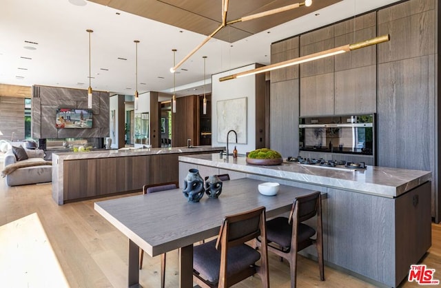 kitchen featuring a spacious island, light hardwood / wood-style floors, hanging light fixtures, oven, and stainless steel gas stovetop