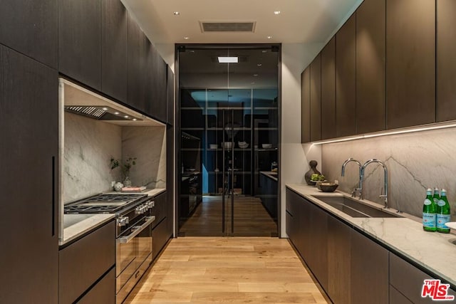 kitchen featuring backsplash, light wood-type flooring, light stone countertops, high end stainless steel range, and sink