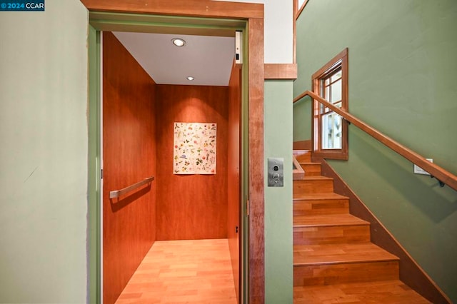 stairway with wood-type flooring, wooden walls, and elevator