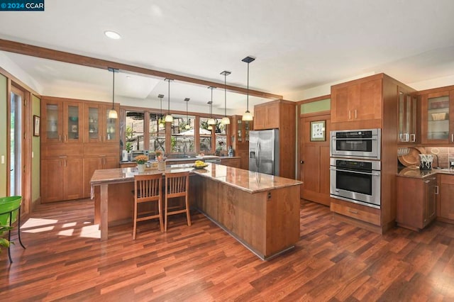 kitchen featuring stainless steel appliances, light stone counters, hanging light fixtures, and dark hardwood / wood-style flooring