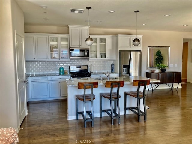 kitchen featuring hanging light fixtures, a kitchen island with sink, stainless steel appliances, light stone countertops, and a kitchen bar