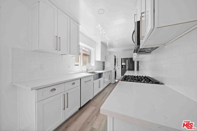 kitchen featuring light wood-type flooring, stainless steel appliances, backsplash, and white cabinets