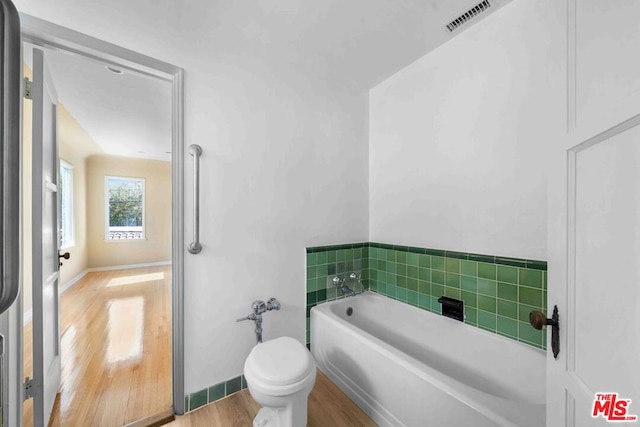 bathroom with a tub to relax in, toilet, and hardwood / wood-style floors