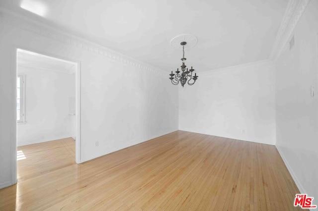 empty room featuring light wood-type flooring, a notable chandelier, and ornamental molding