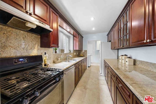 kitchen with black gas range, backsplash, stainless steel dishwasher, light stone counters, and sink