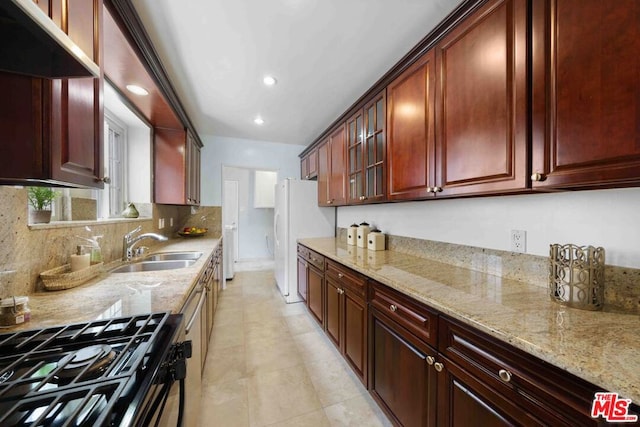 kitchen with light stone counters, sink, black gas stove, and white fridge