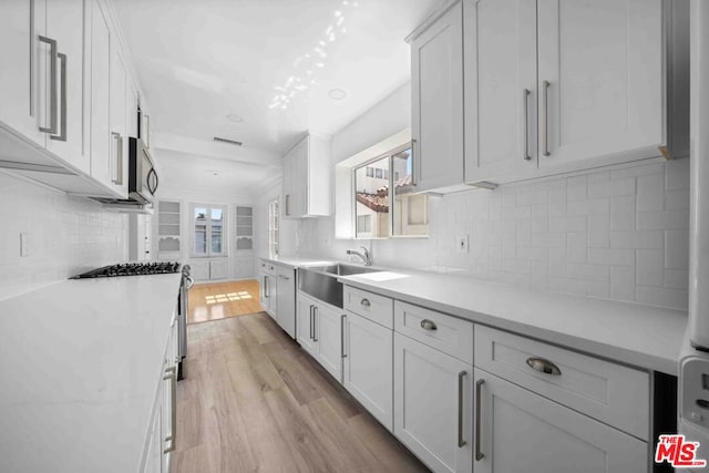 kitchen with light wood-type flooring, appliances with stainless steel finishes, white cabinets, and sink