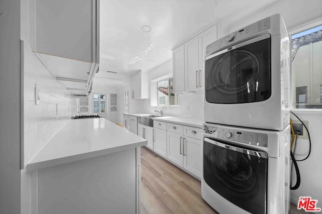 laundry area with sink, stacked washer and clothes dryer, and light wood-type flooring