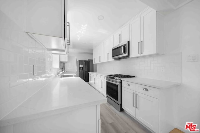 kitchen with stainless steel appliances, light hardwood / wood-style floors, white cabinetry, and sink