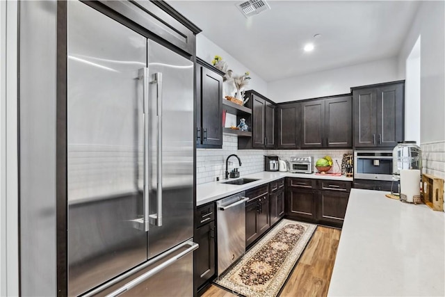 kitchen with sink, dark brown cabinets, appliances with stainless steel finishes, light hardwood / wood-style floors, and decorative backsplash