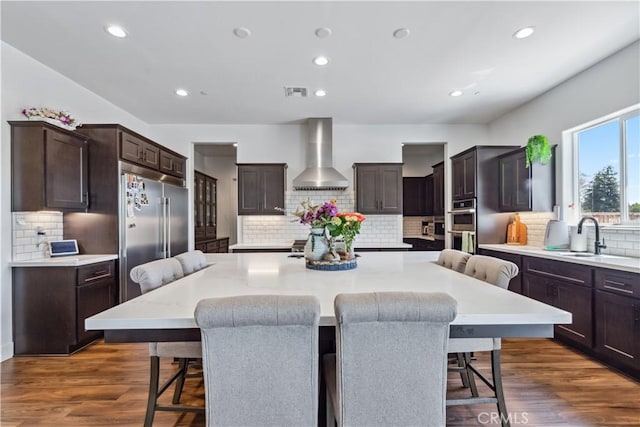 kitchen featuring appliances with stainless steel finishes, a breakfast bar area, wall chimney range hood, and a spacious island