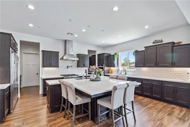 kitchen with light hardwood / wood-style flooring, a center island with sink, a kitchen bar, and wall chimney exhaust hood