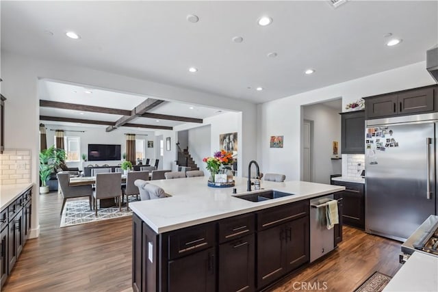 kitchen featuring appliances with stainless steel finishes, dark hardwood / wood-style floors, sink, a kitchen island with sink, and beam ceiling