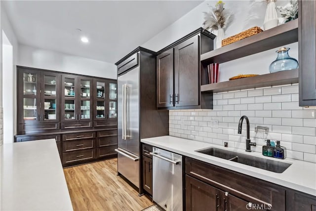 kitchen with sink, dishwasher, dark brown cabinets, light hardwood / wood-style floors, and decorative backsplash