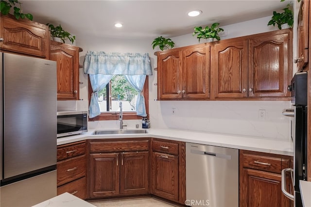 kitchen featuring recessed lighting, stainless steel appliances, a sink, light countertops, and brown cabinetry