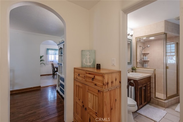 bathroom featuring wood finished floors, vanity, baseboards, ornamental molding, and a shower stall