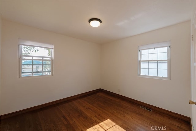 unfurnished room featuring dark wood-type flooring, visible vents, and baseboards