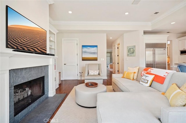 living room featuring dark hardwood / wood-style floors, built in features, crown molding, and a tiled fireplace