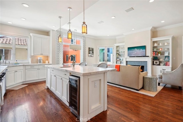 kitchen featuring white cabinets, an island with sink, beverage cooler, and hanging light fixtures