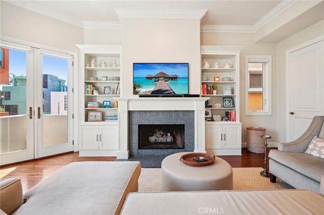 living room featuring built in features, wood-type flooring, crown molding, and a tiled fireplace