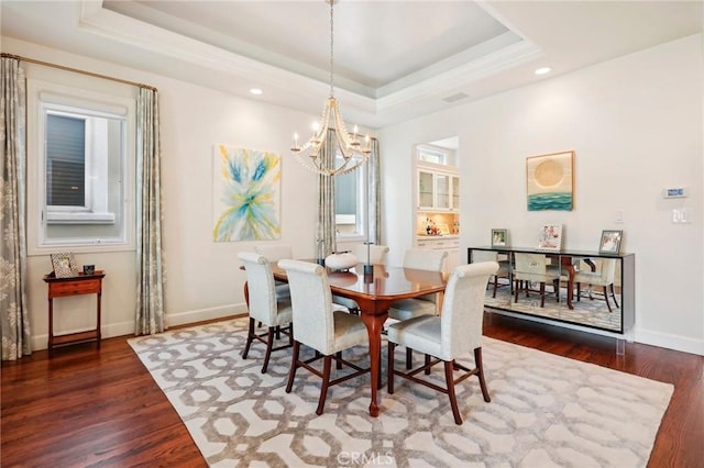 dining space featuring a tray ceiling, dark wood-type flooring, and a notable chandelier