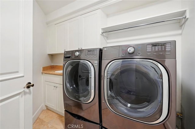 clothes washing area featuring washing machine and dryer, light tile patterned flooring, and cabinets