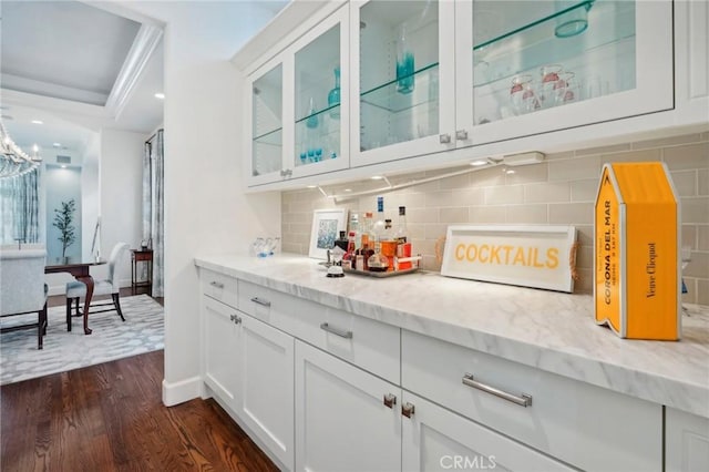 bar featuring decorative backsplash, white cabinetry, dark wood-type flooring, and light stone counters