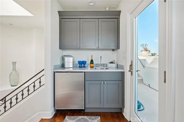 bar featuring stainless steel fridge, gray cabinetry, dark wood-type flooring, and sink