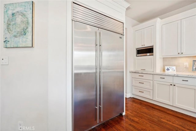 kitchen with light stone countertops, dark hardwood / wood-style flooring, backsplash, built in appliances, and white cabinets