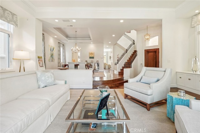 living room featuring an inviting chandelier, light hardwood / wood-style floors, ornamental molding, and a raised ceiling